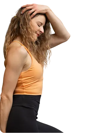 Kobieta w pomarańczowym topie sportowym i czarnych legginsach, z dłońmi we włosach, uśmiechnięta w profilu.