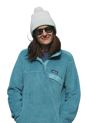 Uśmiechnięta kobieta w jasnej czapce zimowej, okularach przeciwsłonecznych i turkusowej polarowej bluzie.