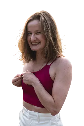 Uśmiechnięta kobieta w bordowym topie i białych spodniach patrzy w stronę obiektywu.